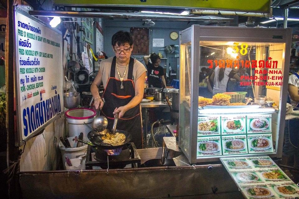 Thai street food vendor cooking noodles, with Thai-language menu signage